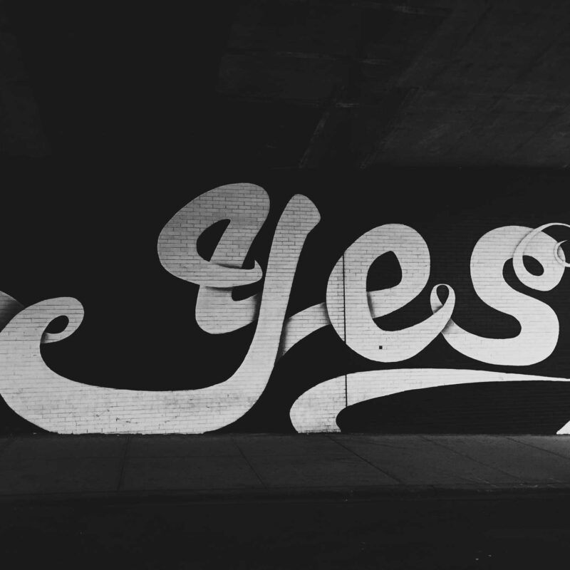 A big white typographic 'Yes' painted on a black brick wall.