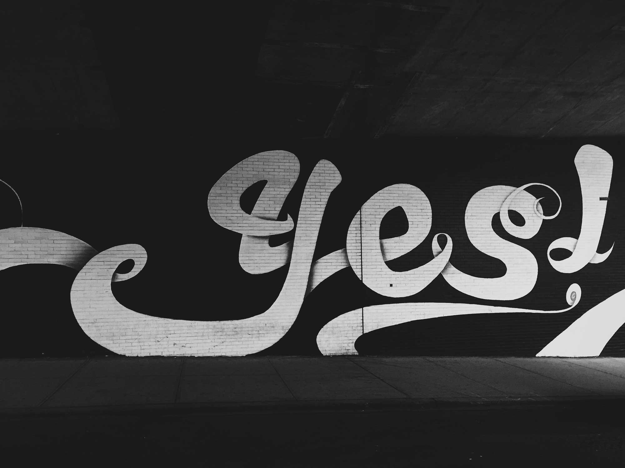 A big white typographic 'Yes' painted on a black brick wall.