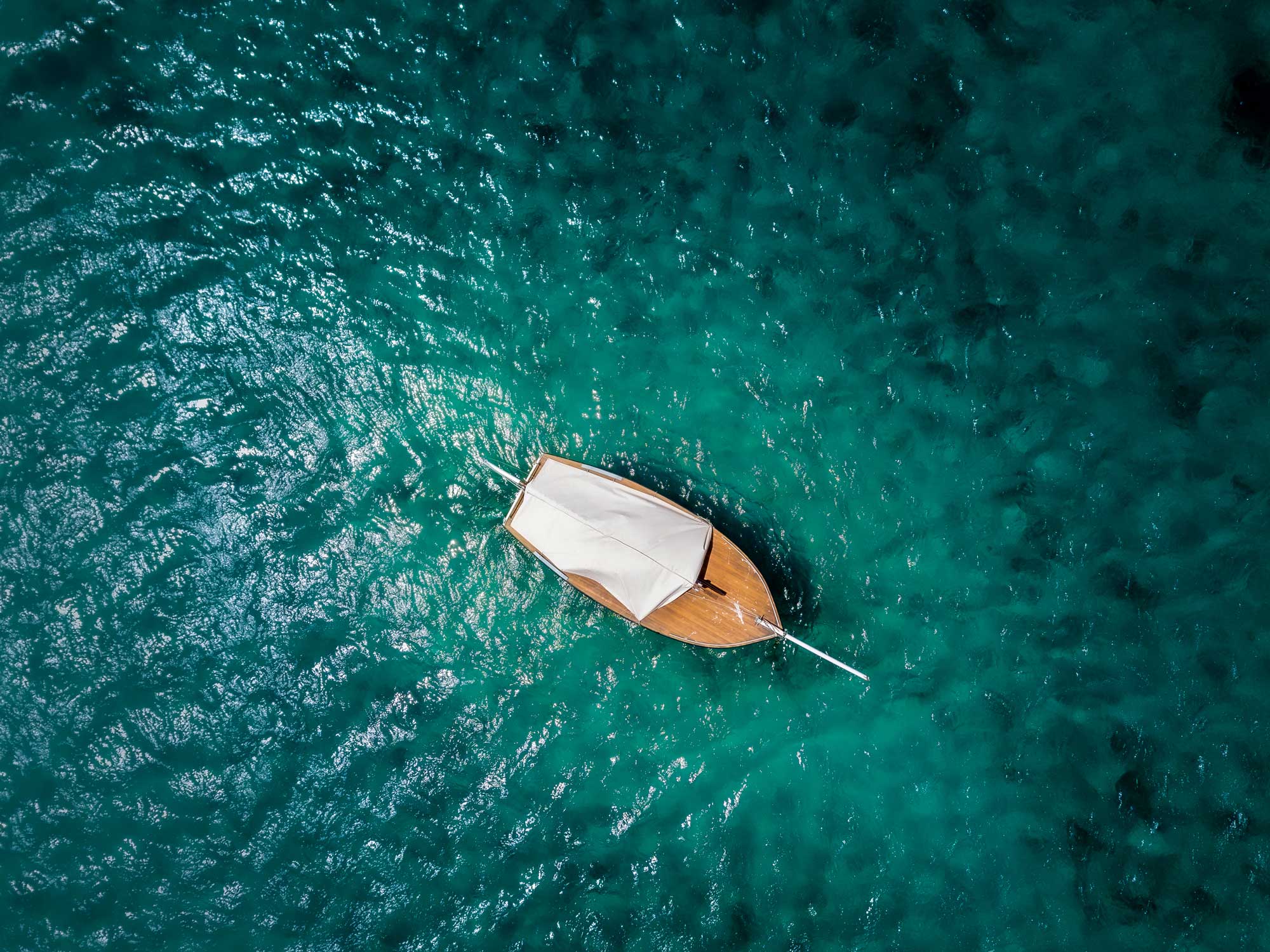 A bird's eye view of a wooden boat drifting in the ocean.