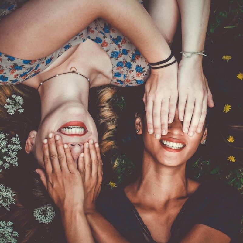 Two young woman cover their eyes in anticipation and expectancy.