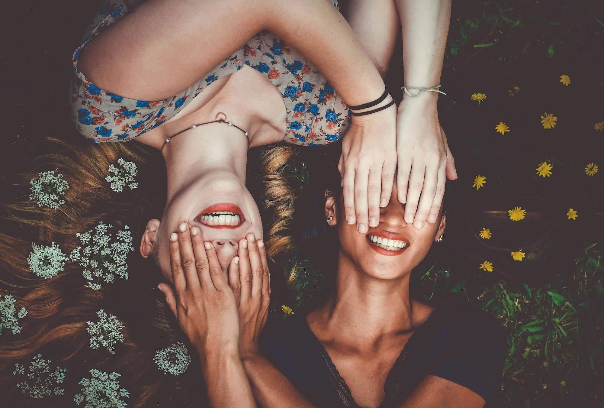 Two young woman cover their eyes in anticipation and expectancy.